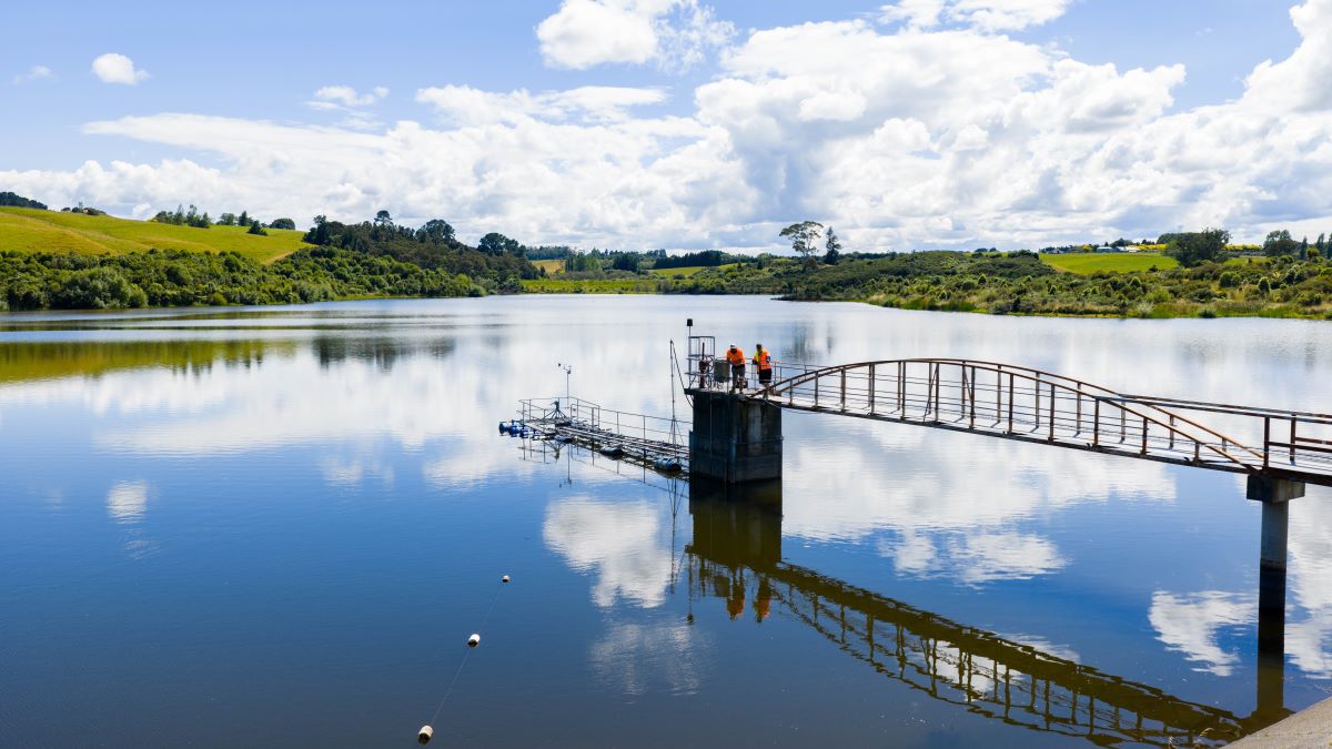 A steel bridge stretches out over a lake of water and is reflected back.
